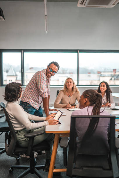 Black Manager Speaking to Female Employees Indoor shot of a work meeting. Cheerful black manager speaking to female employees. Short hair woman taking notes and using a digital tablet. workplace diversity vertical stock pictures, royalty-free photos & images