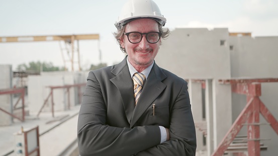 Investor or businessman or real estate business owner have leadership and vision, standing at construction site of real estate projects in urban areas. Male construction manager in suit with helmet crossed arm, smiling and looking at camera.