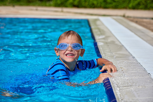 Happy little Caucasian boy swims and dives, has fun in the pool in protective glasses. Independent cute child boldly dives in the pool on summer vacation