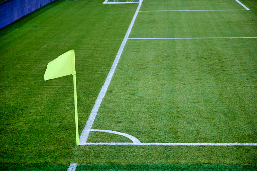 On right corner of the football field there is a green flag on the flagpole. Corner flag as a special element of marking is used by the referee of the match on football with insufficient visibility