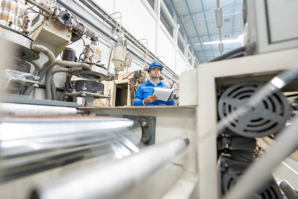 istock American male engineer Standing in control near a machine that is producing plastics and steel. in an industrial warehouse holding a listnote and a walkie-talkie Wear uniforms and helmets. 1492779089
