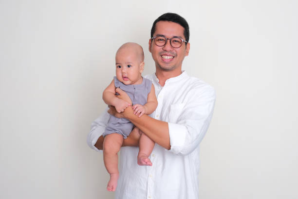 A father smiling happy while holding his baby son A father smiling happy while holding his baby son keluarga stock pictures, royalty-free photos & images
