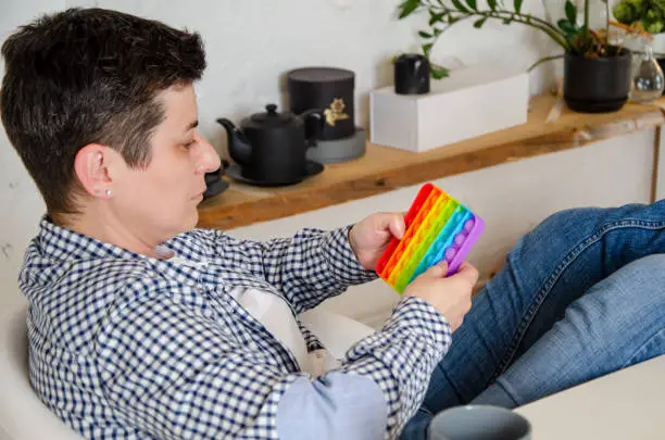 Photo of woman holds an antistress toy in hand. Rainbow Pop-it. relieve stress. Taking break from office work