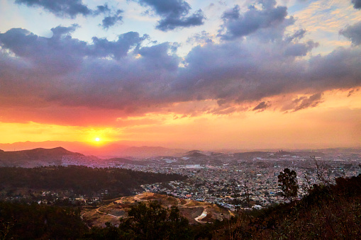 Vista aérea del estado de México, sol en el horizonte y cielo dramático con nubes, Tultitlán visto desde la sierra de Guadalupe, montañas rodeadas por ciudad