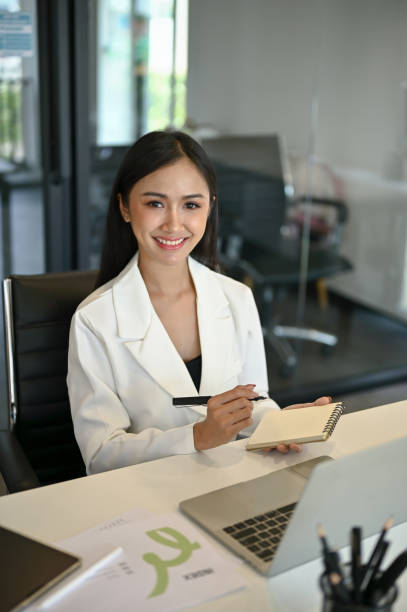 A female assistant or secretary sits at her desk with her notebook and pen in her hands. stock photo