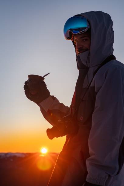 istock Young man in goggles, a jacket and ski gloves drinking tea at sunset 1492795463