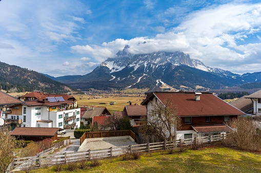 A scenic view of rural houses against Zugspitze on a cloudy sunny day in Germany