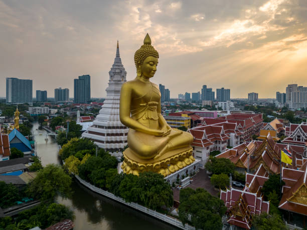 лодка проезжала мимо статуи большого будды (phra buddha dhammakaya thepmongkhon) в храме ват пак нам фаси чароен, расположенном у реки во время заката. - ват стоковые фото и изображения