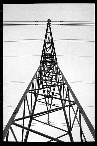 Black and white photograph of a power line tower with multiple interconnected high voltage wires running across the frame