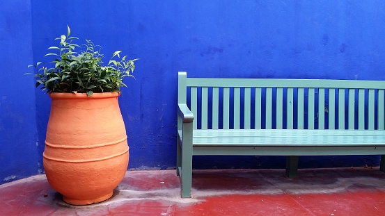 A green bench and pot sitting outside a blue wall next to a large planter