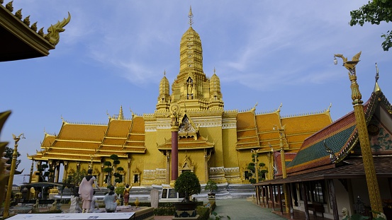 Bangkok, Thailand – December 02, 2022: A majestic yellow temple building with intricate spires and intricate architectural details, set against a bright blue sky in Bangkok