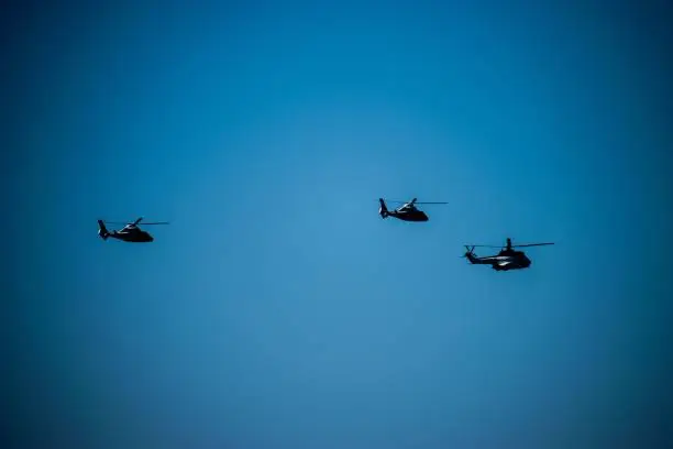 An aerial view of multiple black helicopters flying in unison in a sunny sky