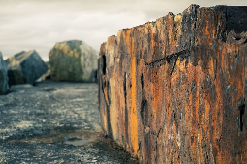 A weathered, concrete fence post rests on a beach, surrounded by rust and texture