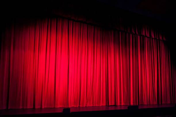 istock Illuminated theatrical stage with a voluminous draped red curtain 1492803514
