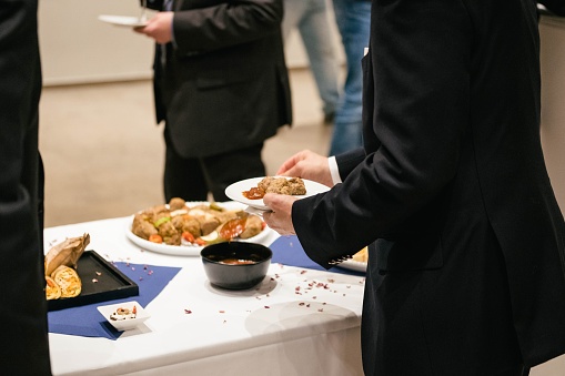 People in suits serve themselves at the buffet and eat delicious food at a business event. There are snacks and finger food.