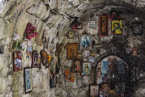 A picturesque stone wall adorned with a variety of intricate religious paintings and photographs, located inside a cave