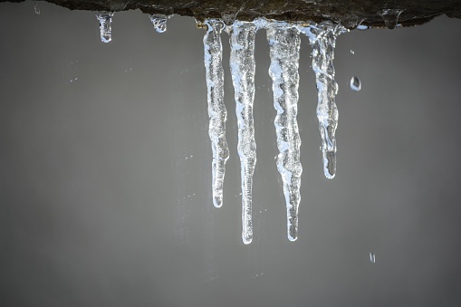 A set of icicles hang from an industrial pipe on the side of a building