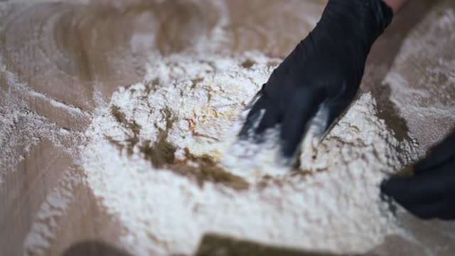 Close-up mixing flour with egg on wooden table indoors. Unrecognizable female cook in gloves blending ingredients in kitchen baking tasty food.