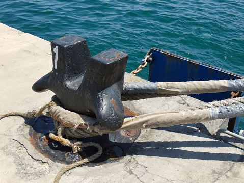 A rope tied securely around a metal post on the deck of a sailing vessel, creating an anchor line to keep the ship in place
