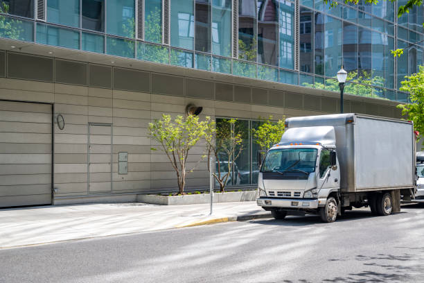 istock Light gray cab over small rig semi truck with box trailer making delivery to multilevel apartment building in urban city 1492810277