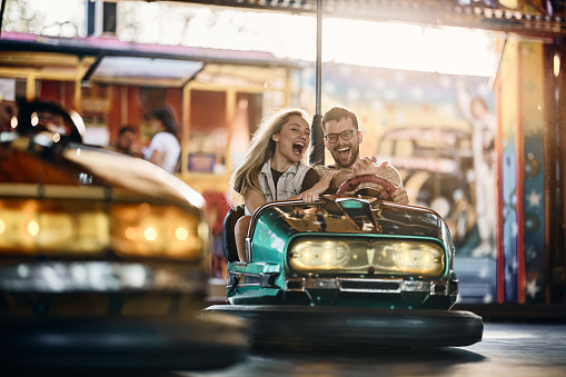Young happy couple having fun in bumper car at amusement park.