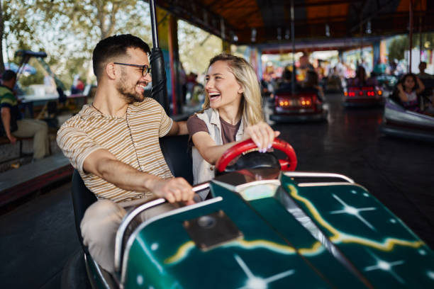 istock Young cheerful couple talking during bumper car ride at amusement park. 1492811070