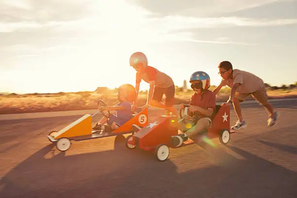A group of young neighborhood boys race into the sunset for the go-cart street championship.