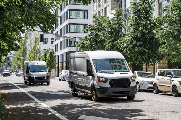 Commercial cargo mini vans making deliveries driving on the urban city street with multilevel apartment buildings stock photo