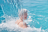 Senior caucasian smiling woman with gray hair enjoying falling on her shoulders flow of water.
