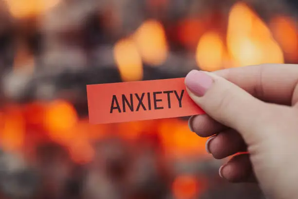 Photo of Red paper with inscription Anxiety in woman's hand near bonfire