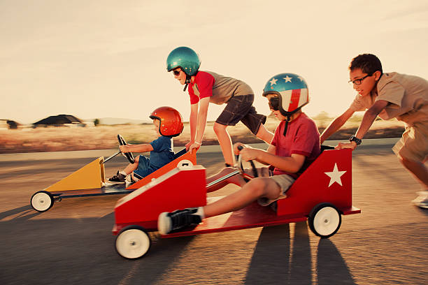 Winning by a Nose A group of young neighborhood boys race into the sunset for the go-cart street championship. soapbox cart stock pictures, royalty-free photos & images