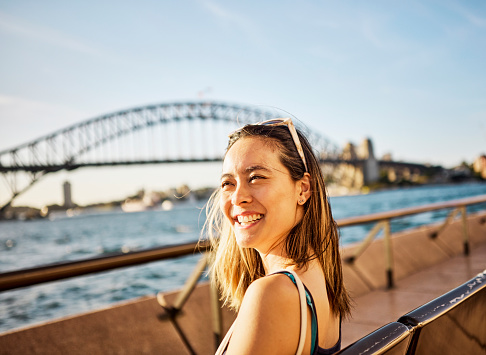 An Asian solo traveller sits admiring the breathtaking sea view of Sydneys cityscape, standing testament to Australias impressive architecture.