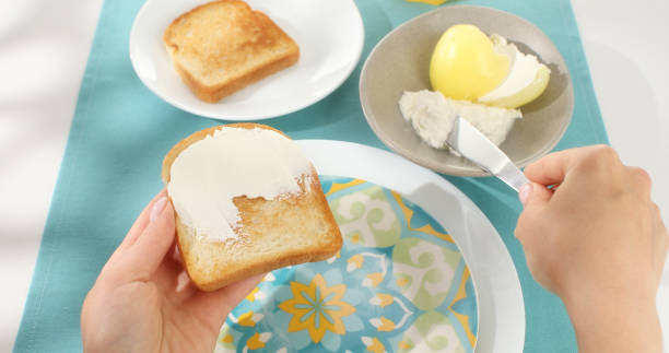 spreading cream cheese on toast. white and blue background. pov. top view.