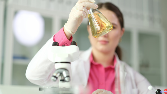 Scientist chemist looking at flask with yellow liquid or oil for transparency in chemical laboratory closeup. Machine oil quality control concept