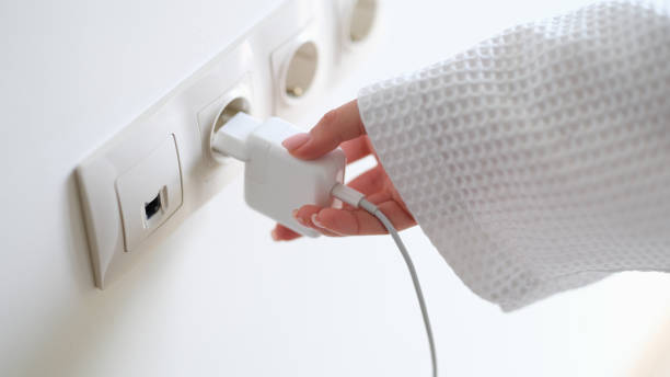 istock Woman in white bathrobe inserting plug into outlet at home with hand closeup 1492830343