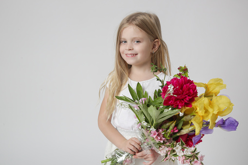 Studio portrait of beautiful little girl holding big colorful bouquet of various flowers.