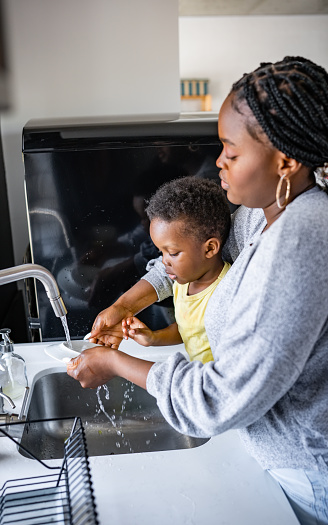 African-American mother and cute little son wasing dishes together. Helping hand. House chores and early education.