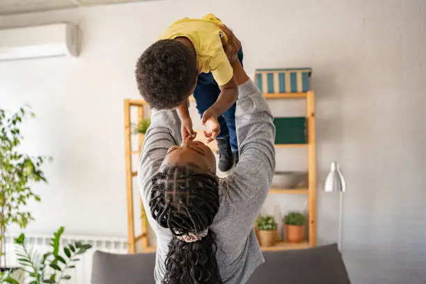 Cheerful African-American mother and cute toddler son dancing at home. Mother-son fun bonding time