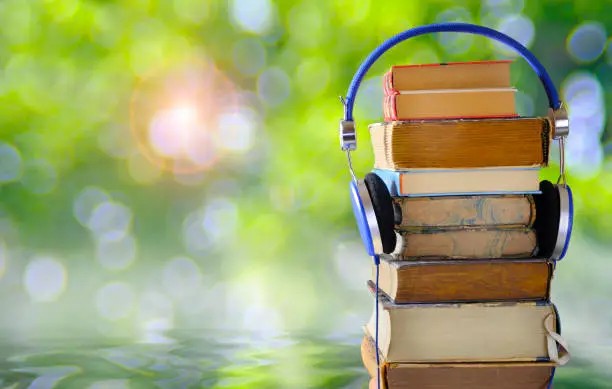 Photo of Relaxing with audiobooks during summer holidays with heap of books and vintage headphones. Beautiful blurred rising sun and nature background