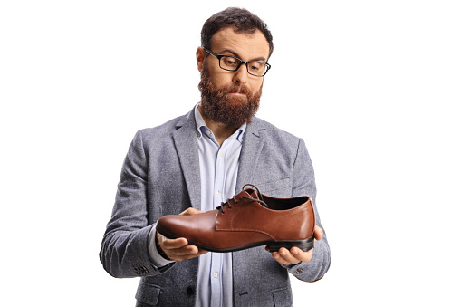 Confused bearded man holding a brown leather shoe isolated on white background