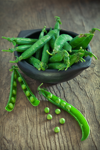 Beautiful fresh English Peas in pods and shucked from their pod on wood.  Shallow dof
