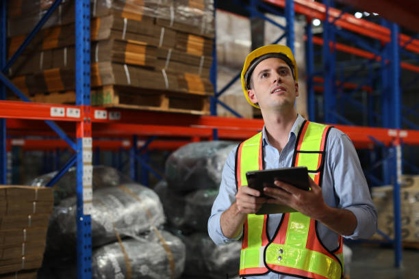 istock Warehouse workers manwith hardhats and reflective jackets using tablet, walkie talkie radio and cardboard while controlling stock and inventory in retail warehouse logistics, distribution center 1492837202