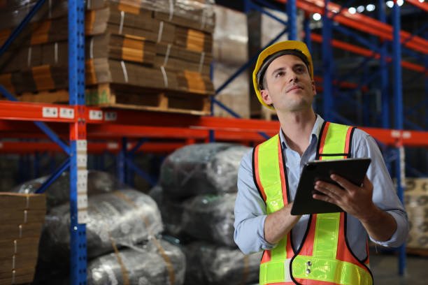 istock Warehouse workers man with hardhats and reflective jackets using tablet, walkie talkie radio and cardboard while controlling stock and inventory in retail warehouse logistics, distribution center 1492837477