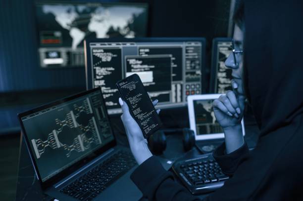 istock Holding smartphone with code. Young professional female hacker is indoors by computer with lot of information on displays 1492839407