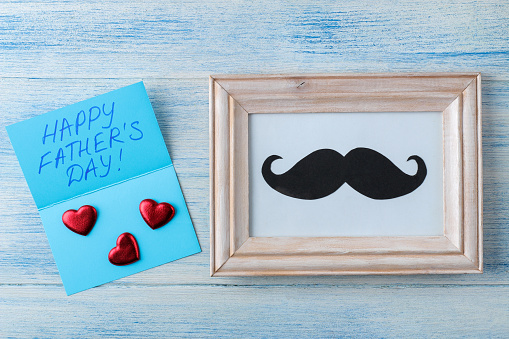 happy father's day. decorative male mustache in a frame on a light blue wooden background. top view