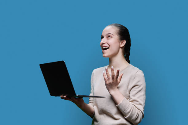 istock Surprised teen girl using laptop on blue studio background 1492845497