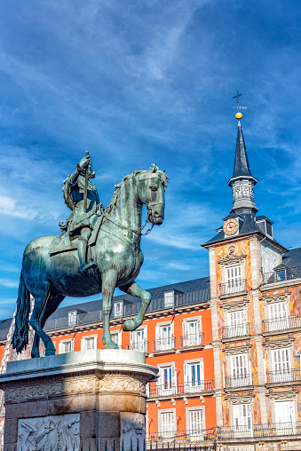 The bronze statue represents Felipe II mounted on horseback. It is placed in the centre of Plaza Mayor in Madrid and it is here represented with the clock tower as a backdrop on a partially cloudy sky during daytime.