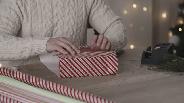 Close up shot of young man wrapping a cute little gift box in a candy cane wrapping paper