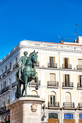The statue  of Carlos II stands majestic in front of the white buildings surrounding Puerta del Sol in Madrid.