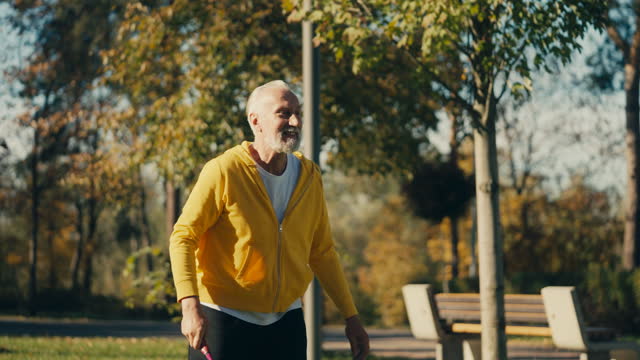 Smiling man in his 60s playing badminton in autumn park, outdoor activity, rest
